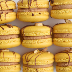 Chocolate banana French macaron featuring yellow macaron shells, chocolate drizzle, filled with a chocolate ganache and banana buttercream.