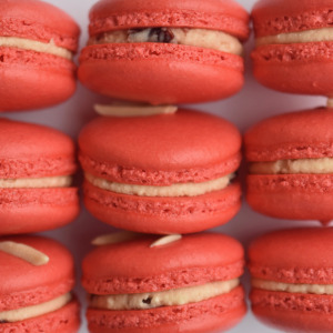 Cherry almond French macaron featuring red macaron shells and an almond sliver on top. Filled with cherry almond buttercream.