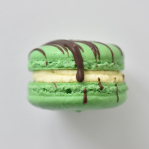Mint chocolate chip French macaron featuring green macaron shells topped with a chocolate drizzle, filled with a mint chocolate buttercream.