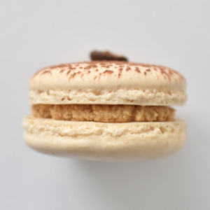 Tiramisu French macarons featuring cream macarons shells topped with a coffee bean and dusted with cocoa powder. Filled with a tiramisu flavored buttercream.