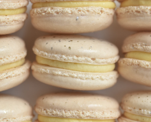 Champagne French macaron featuring cream macaron shells topped with silver and gold paint splatters. Filled with a champagne buttercream.