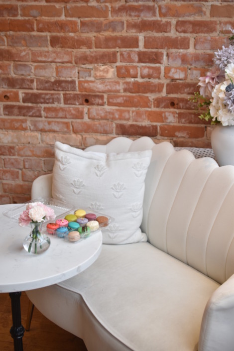 Interior View of LBM Holland An interior view of the Le Bon Macaron Holland storefront, featuring the exposed brick, cream couch, and marble table.