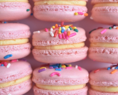 Pink French macarons topped with rainbow sprinkles, filled with a sugar cookie buttercream.
